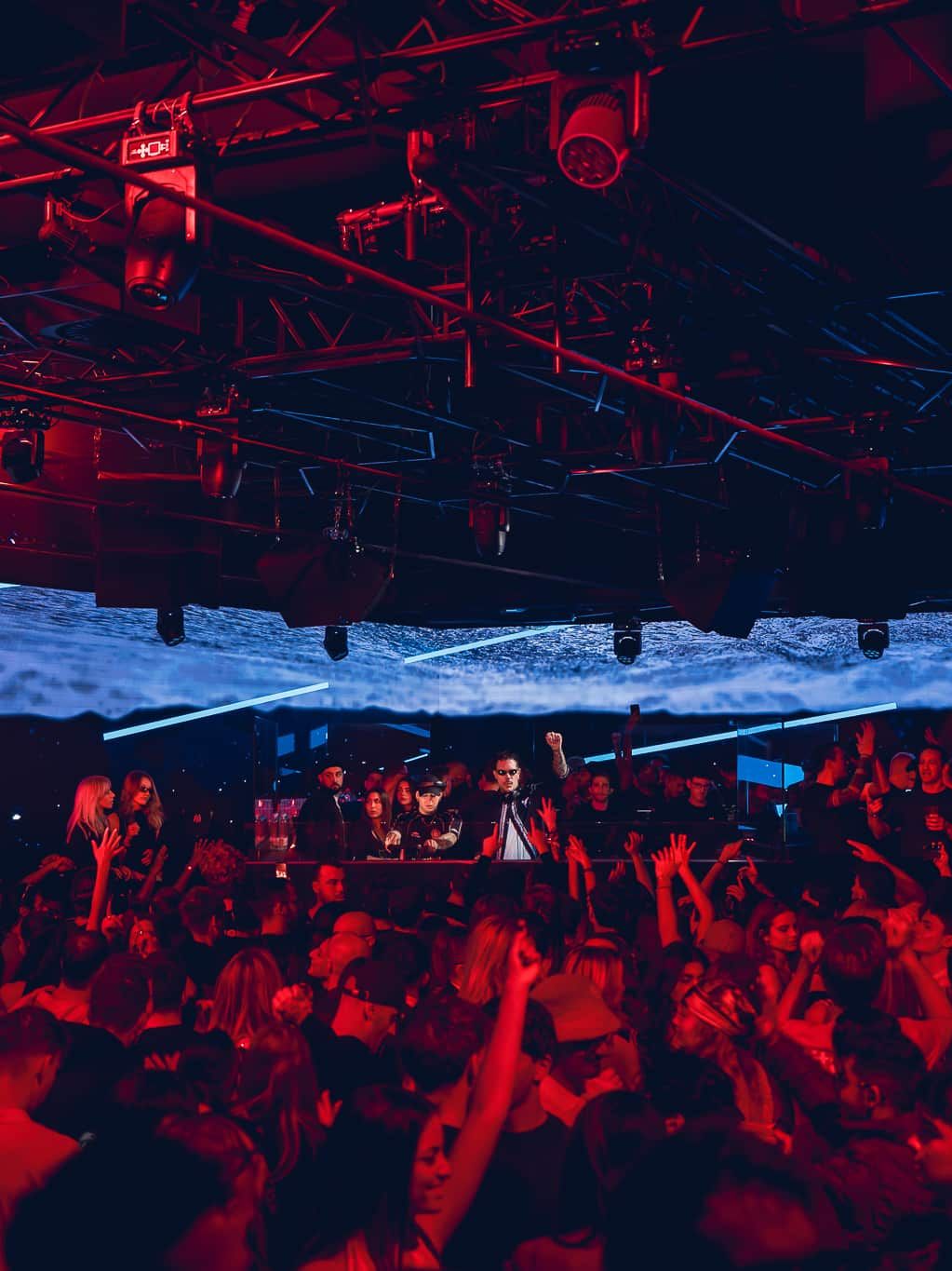 Una discoteca affollata con gente che balla sotto luci rosse e blu, un DJ che si esibisce sul palco, a catturare l'energia vibrante di una vera discoteca milanese. Amnesia Milano